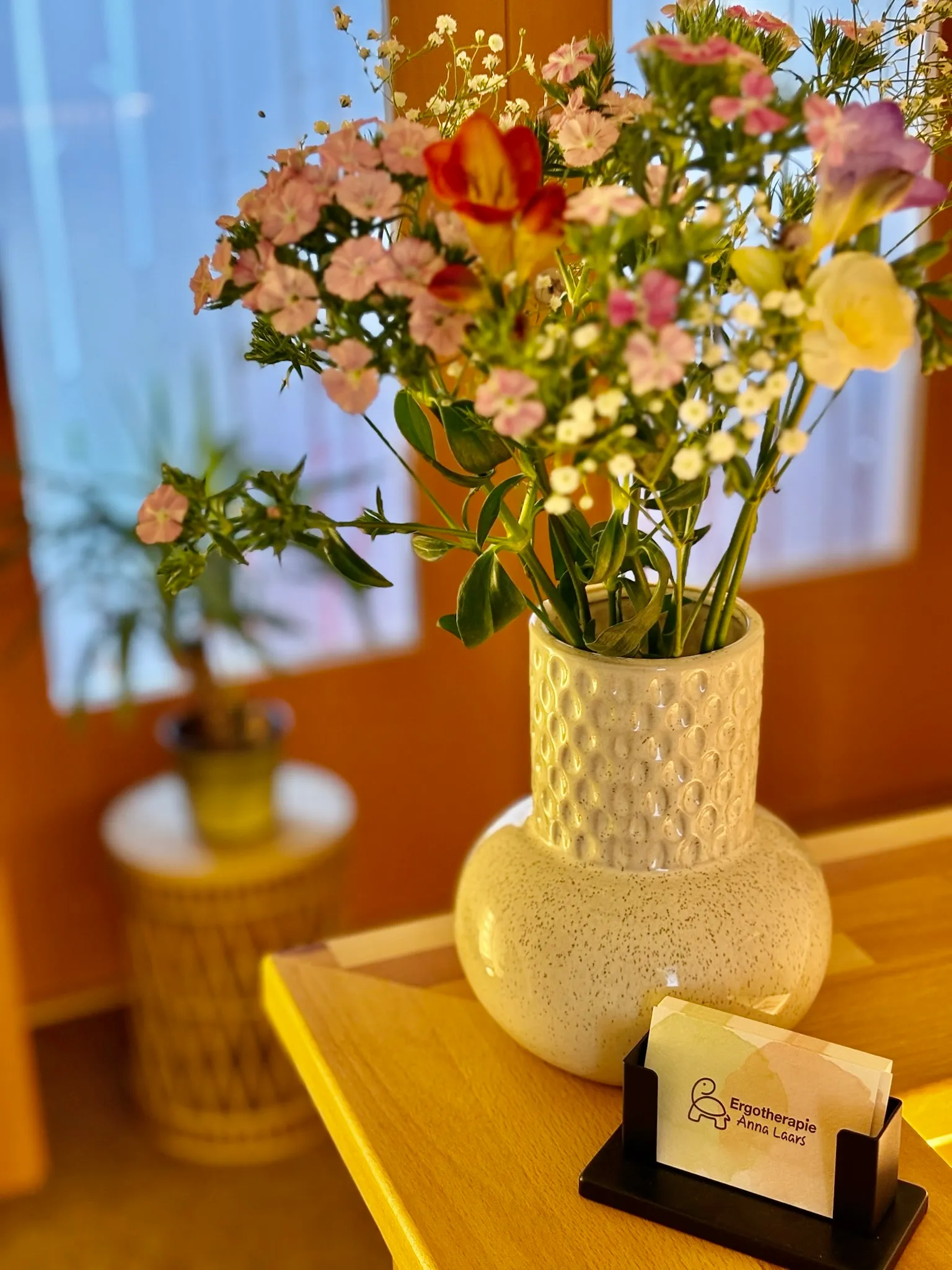Blumenstrauß in einer hellen Vase auf dem Empfangstresen, daneben Visitenkarten der Praxis